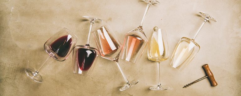 Flat-lay of red, rose and white wine in glasses and corkscrews over grey concrete background, top view, wide composition. Wine bar, winery, wine degustation concept